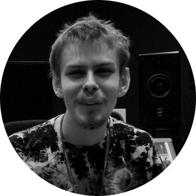Black and white picture of Marshall smiling with the backdrop of a studio monitor speaker behind him.