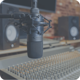 A high-quality studio microphone mounted on a shock mount, positioned in front of a large mixing console, with professional studio monitors in the background.